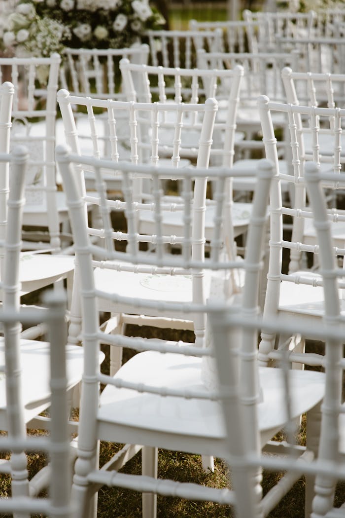 Rows of white chairs arranged outdoors for a wedding ceremony under natural sunlight.