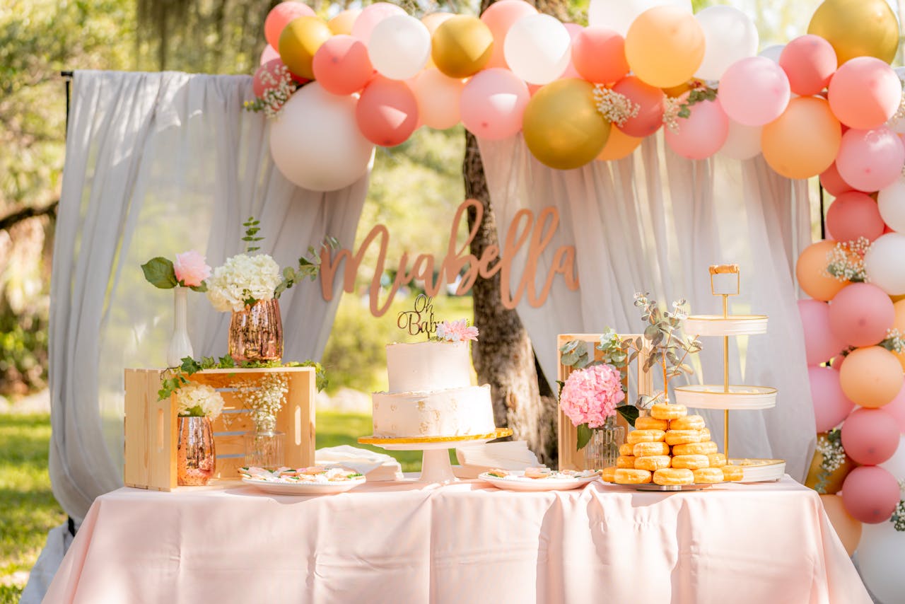 Delightful baby shower table with cake, balloons, and dessert display in an outdoor garden setting.